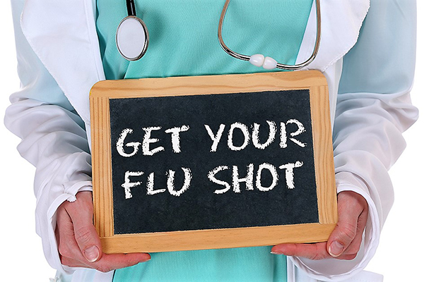 Photo of a nurse holding up a sign GET YOUR FLU SHOT