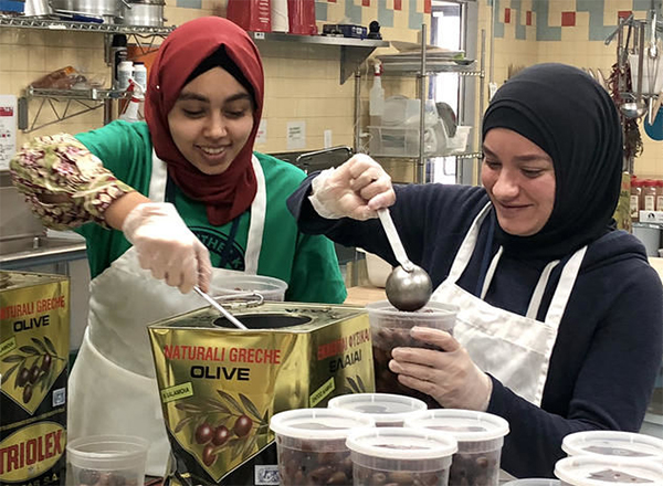 Two volunteers scooping olives into food containers