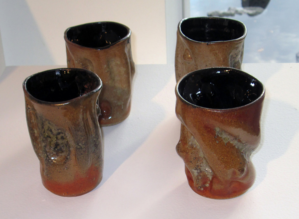 Four ceramic tumblers with abstract indents and bulges, each with black interior glaze and red-brown exterior glaze