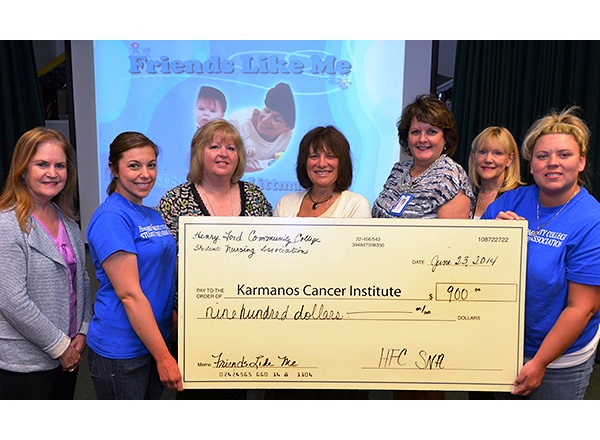 Seven people hold up a check for 900 dollars for the Karmanos Cancer Institute