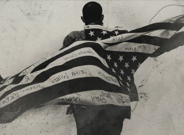 Black man shown from behind with American flag flowing behind him. 