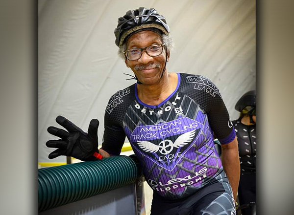 Dr. Gerald Walker is smiling and waving, wearing a bike helmet and pirple and black cyclist gear.